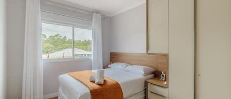 Ein Schlafzimmer mit Bett, Nachttisch, Kleiderschrank und einem Fenster mit Vorhängen.