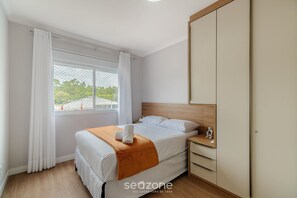 A bedroom with a bed, a nightstand, a wardrobe, and a window with curtains. - Charming apt Just 350m From the Beach! - Vgn0102 (Florianópolis)