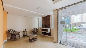 A hotel lobby with two wicker chairs, a small round table, a built-in shelf with a plant, and a glass door leading outside. - Charming apt Just 350m From the Beach! - Vgn0102 (Florianópolis)