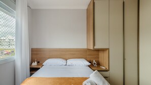 Quarto de hotel com cama, mesa de cabeceira, cabeceira de madeira, guarda-roupa e janela com cortinas.