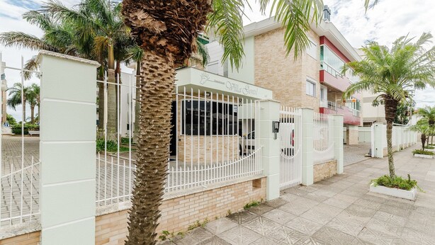A residential building with a gated entrance, a palm tree in the foreground, and a paved walkway. - Charming apt Just 350m From the Beach! - Vgn0102 (Florianópolis)