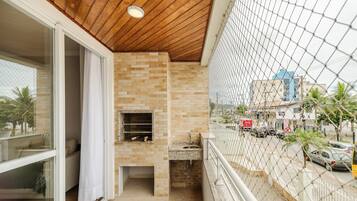 Een balkon met een bakstenen muur, een barbecue en uitzicht op de straat.