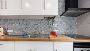 Una cucina con mobili bianchi, un lavello in acciaio inossidabile, una piastrellatura decorata e un bollitore rosso sul piano di lavoro.