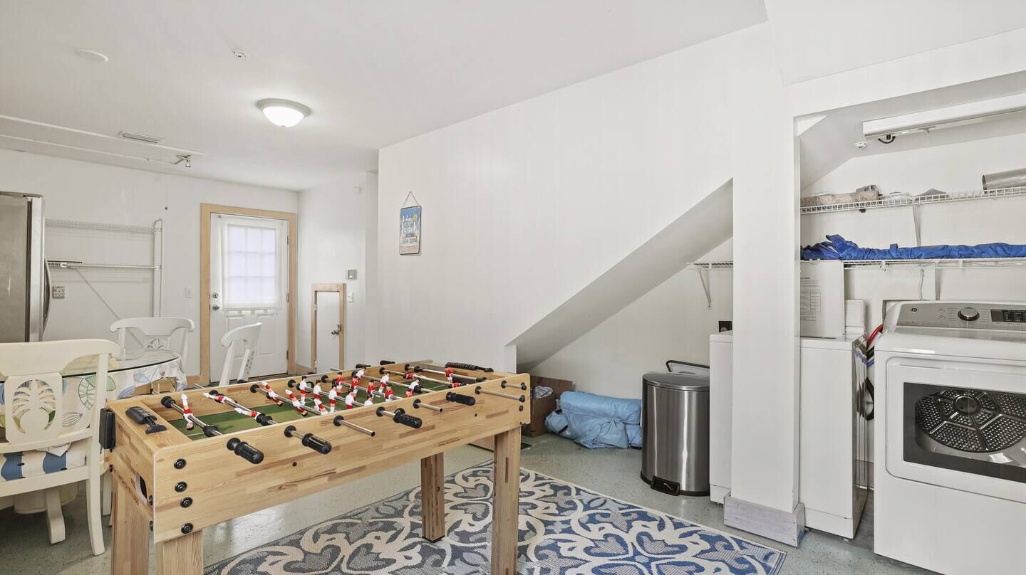 A room with a foosball table, a washing machine, and a kitchen area.