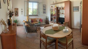 Una sala de estar con una mesa de comedor, sillas de mimbre, un sofá y un televisor.