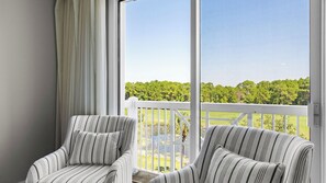 A balcony with two striped chairs, a white railing, and a view of a green landscape.