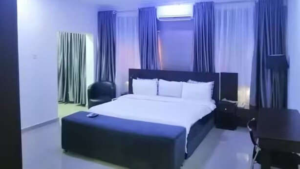 Habitació d'hotel amb un llit gran, una taula de nit, una cadira i un aparell d'aire condicionat.