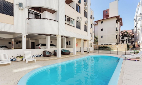 A swimming pool with lounge chairs and a covered area with seating. - Condominium 80m From Praia dos Ingleses - AMC (Florianópolis)