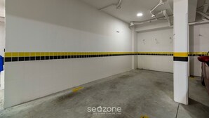 A parking garage with white walls, yellow and black tiled accents, and concrete floors. - Apartment With Barbecue in Itacorubi Aft0210 (Florianópolis)