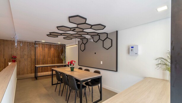 A modern dining area with a wooden table and black chairs, a decorative ceiling light, and a wall-mounted thermostat. - Apartment With Barbecue in Itacorubi Aft0210 (Florianópolis)
