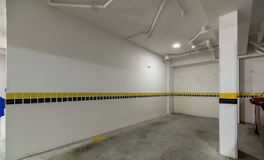 A parking garage with white walls, yellow and black tiled accents, and concrete floors. - Apartment With Barbecue in Itacorubi Aft0210 (Florianópolis)