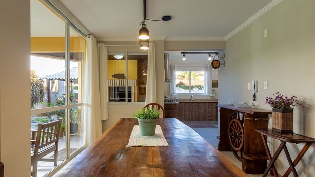 A spacious kitchen with a wooden table, a potted plant, and a large window. - House in Condo w/ Pool, 300m From the Beach Ali024 (Florianópolis)