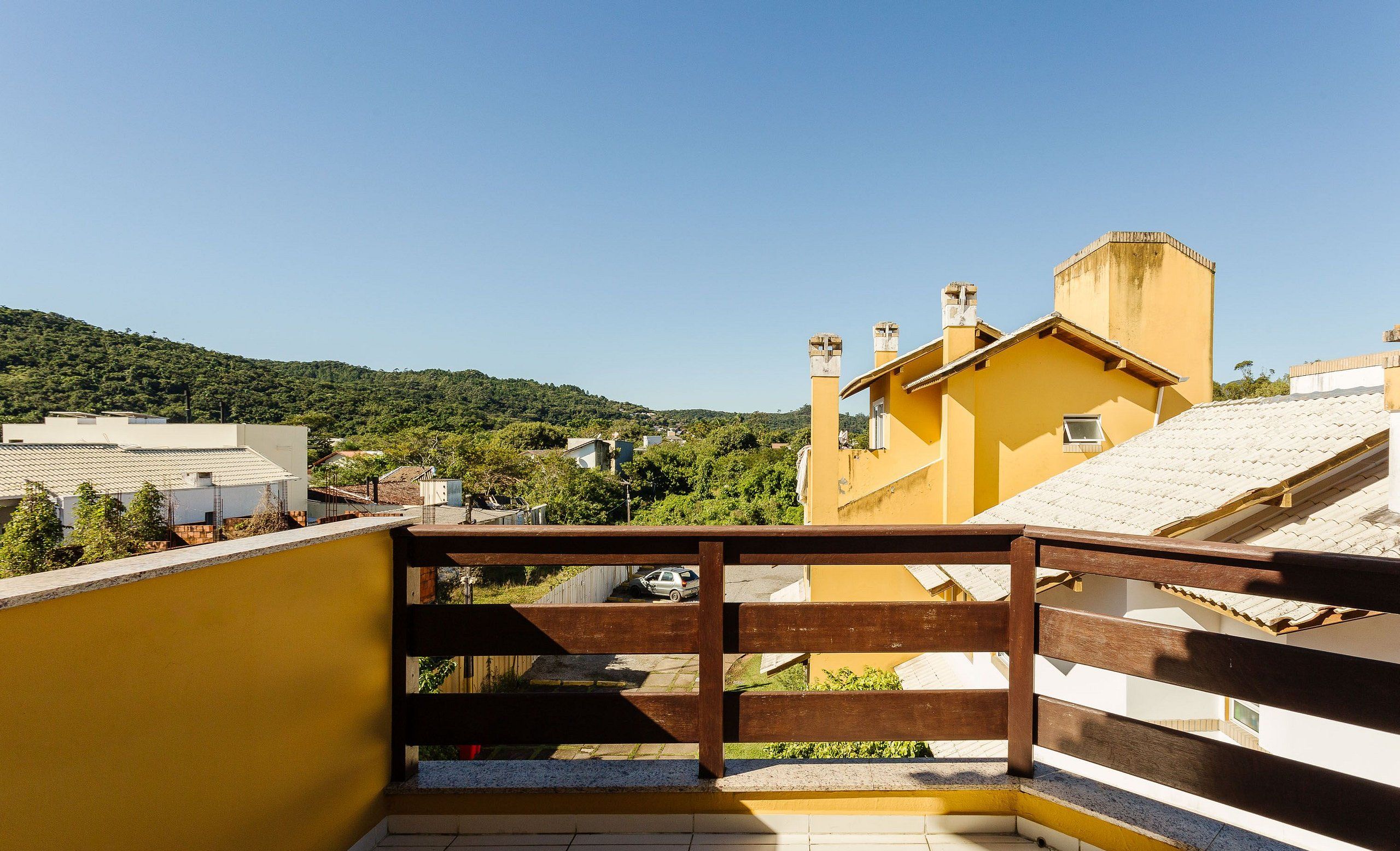 A balcony with a wooden railing overlooking a residential area with houses and greenery.