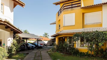 Un barrio residencial con un edificio amarillo, un patio cubierto, coches aparcados y un camino.