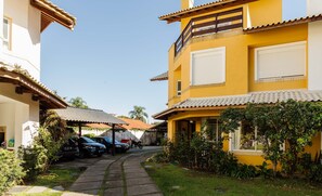 Un barrio residencial con un edificio amarillo, un patio cubierto, coches aparcados y un camino.