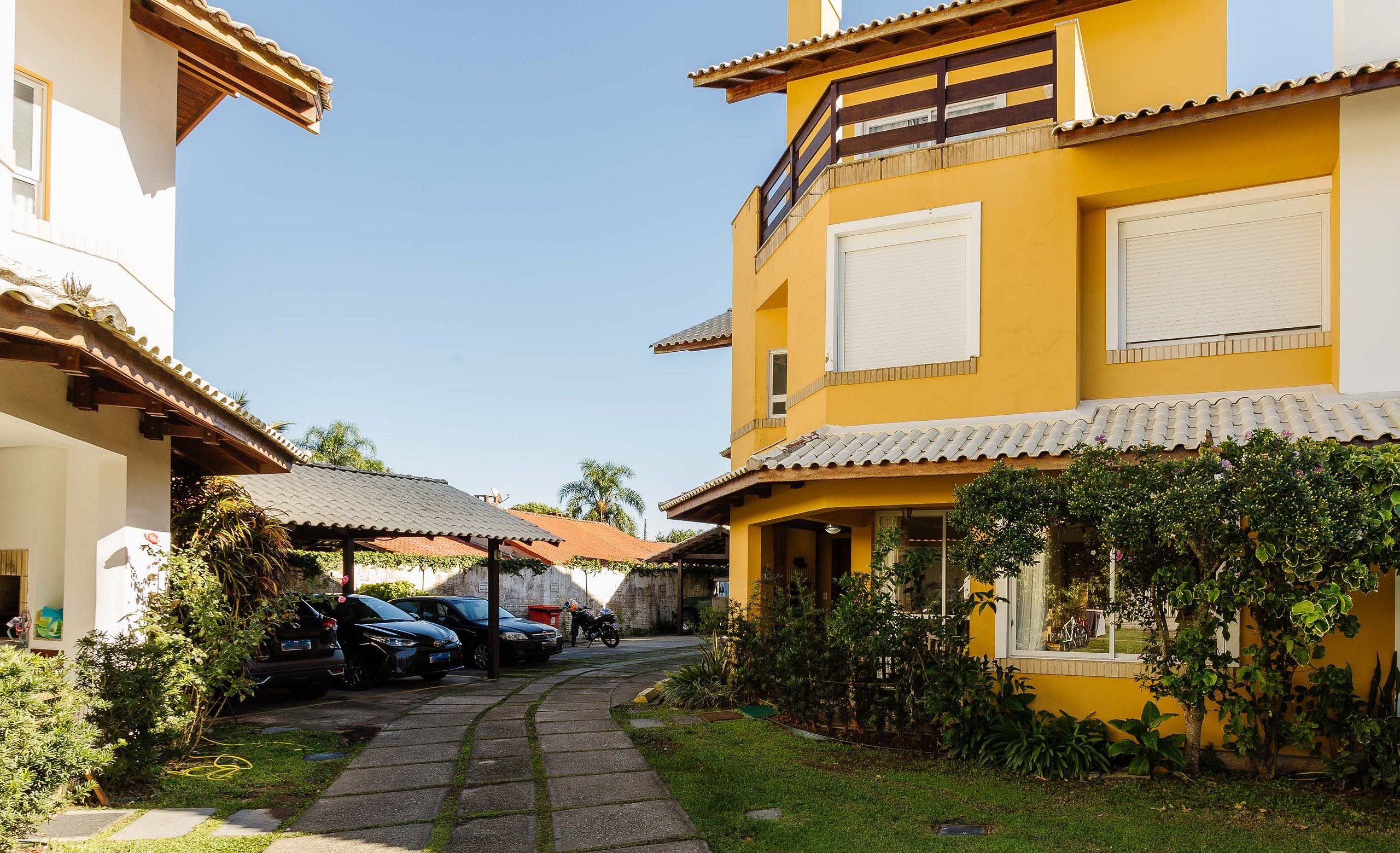 A residential area with a yellow building, a covered patio, parked cars, and a pathway.