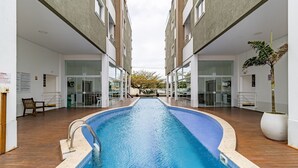 Una piscina con plataforma de madera, rodeada por edificios modernos con puertas y ventanas de vidrio.