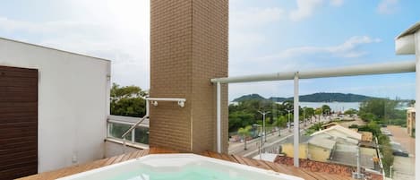 A hot tub on a balcony with a view of a body of water and surrounding buildings.