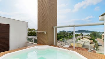 Un jacuzzi en un balcón con vista a una masa de agua y edificios circundantes.