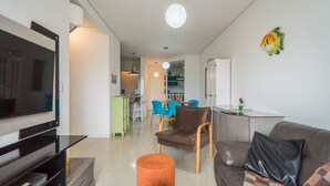 Una sala moderna con un televisor de pantalla plana, un sofá, una mesa de centro y un comedor al fondo.