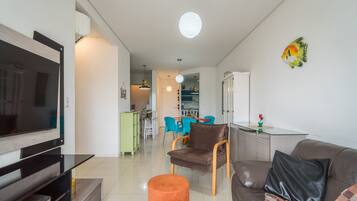 Een moderne woonkamer met een flatscreen televisie, een bank, een salontafel en een eethoek op de achtergrond.