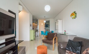Ein modernes Wohnzimmer mit Flachbildfernseher, einer Couch, einem Couchtisch und einem Essbereich im Hintergrund.