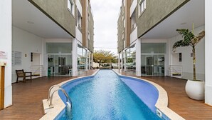 Una piscina con plataforma de madera, rodeada por edificios modernos con puertas y ventanas de vidrio.