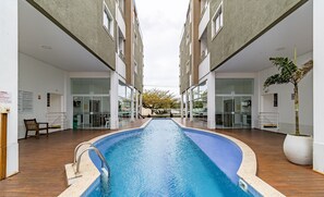Ein Schwimmbad mit Holzterrasse, umgeben von modernen Gebäuden mit Glasfenstern und -türen.