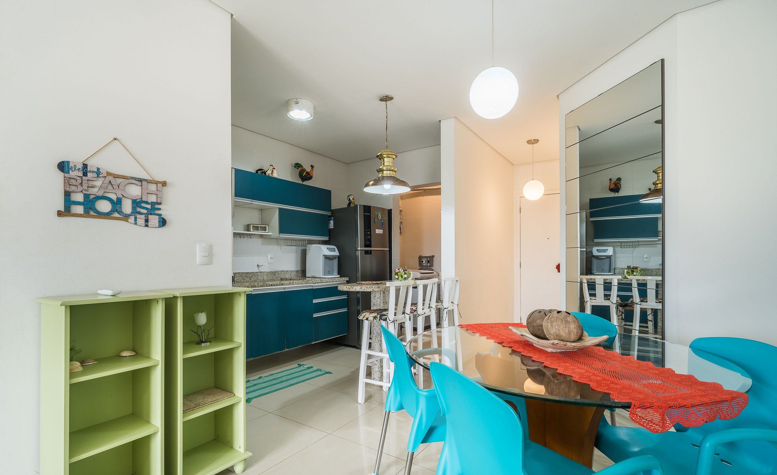 Una cocina moderna con armarios color turquesa, una zona de comedor con sillas azules y un estante verde.