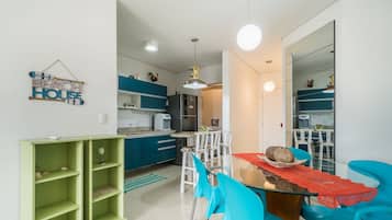 Una cocina moderna con armarios color turquesa, una zona de comedor con sillas azules y un estante verde.