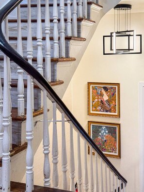 A staircase with white balusters and a black handrail, leading to a landing with a modern light fixture and two framed artworks. - Cozy 4BR City Escape in the Heart of Philly (Philadelphia)