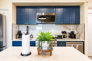 A modern kitchen with dark blue cabinets, a stainless steel range hood, and a marble backsplash. - Cozy 4BR City Escape in the Heart of Philly (Philadelphia)