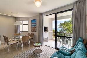 Een moderne woonkamer met een glazen eettafel, rieten stoelen, een bank en uitzicht op de omgeving.