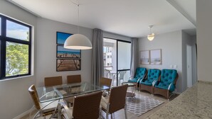 Una sala moderna con una mesa de comedor de vidrio, sillas de mimbre, sofás color turquesa y un balcón con vistas.