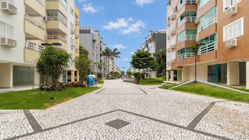 A residential street with modern apartment buildings, a paved walkway, and greenery.