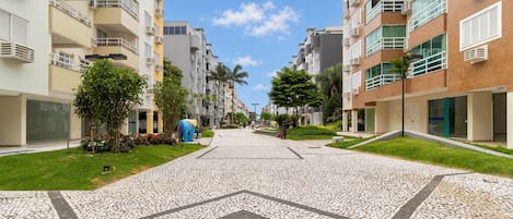 A residential street with modern apartment buildings, a paved walkway, and greenery.