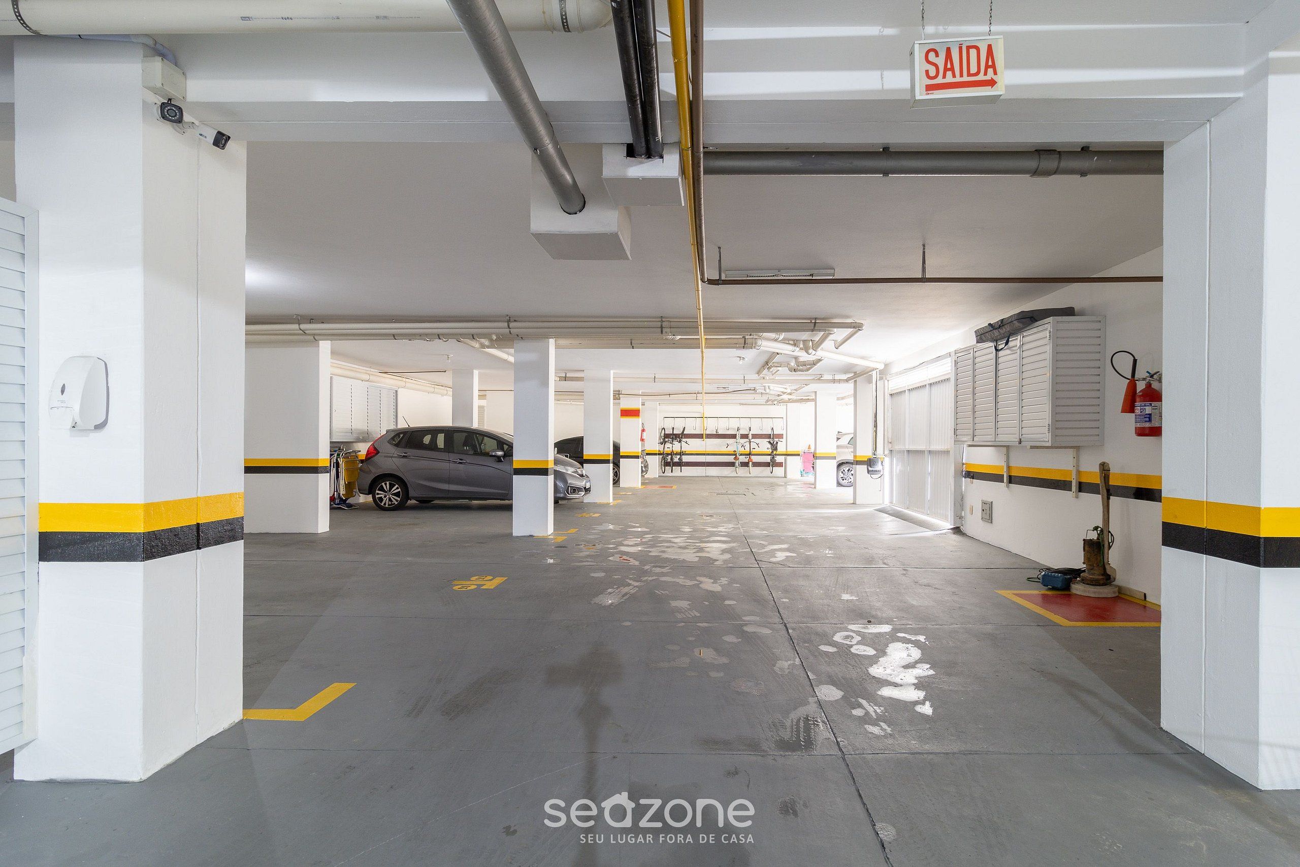 Uma garagem de estacionamento com paredes brancas, listras amarelas e uma placa indicando a saída.