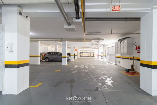 Uma garagem de estacionamento com paredes brancas, listras amarelas e uma placa indicando a saída.