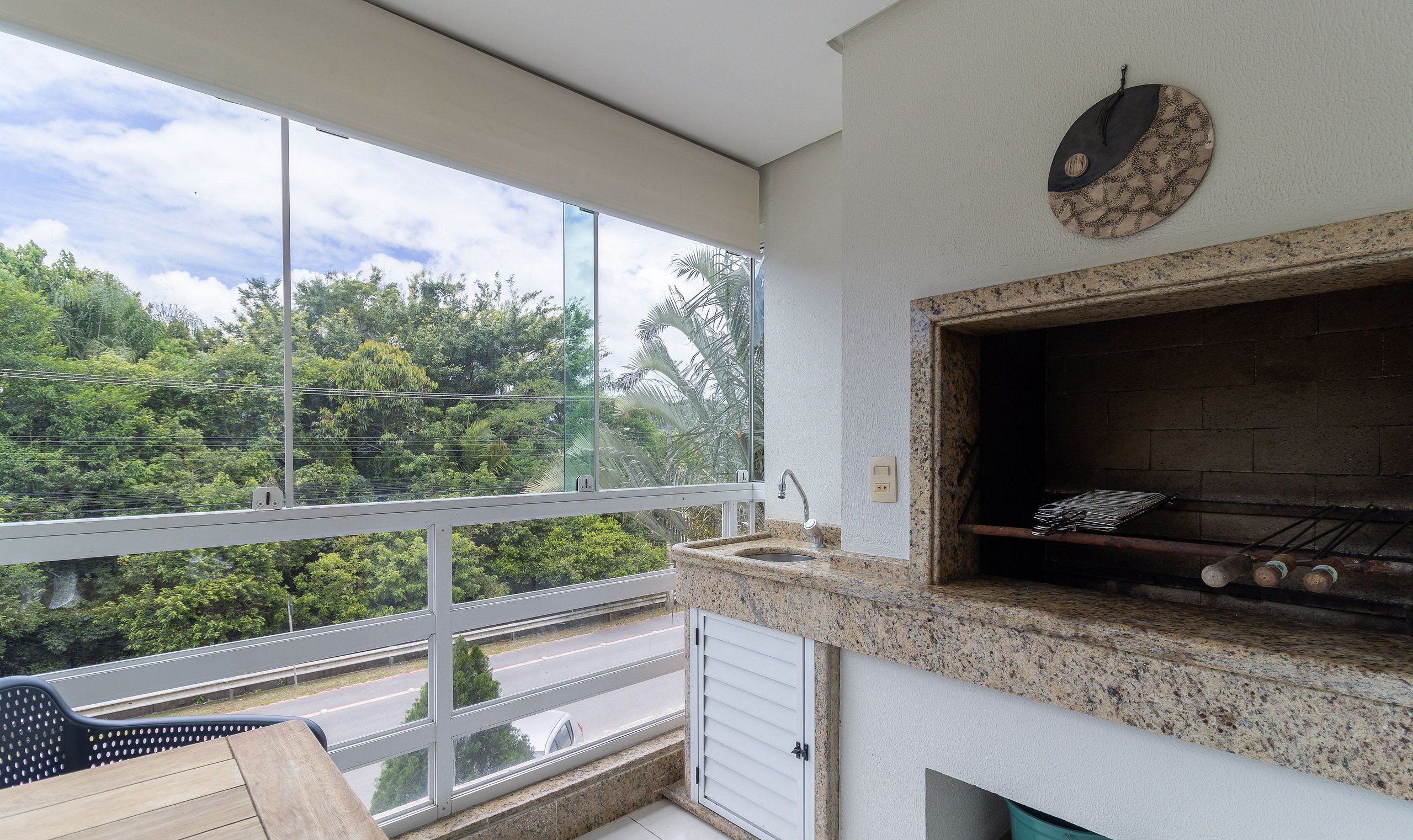 A balcony with a large window overlooking a road and greenery.