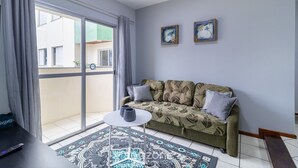 A living room with a sofa, a small table, a patterned rug, and a sliding glass door leading to an outdoor area. - Apt With 3 Bedrooms 200m From Ufsc Elk0101 (Florianópolis)