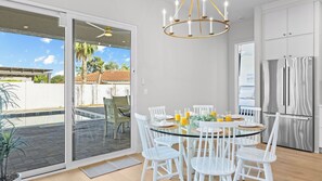 A modern kitchen with a glass dining table, white chairs, a stainless steel refrigerator, and a view of a swimming pool and palm trees. - El Dorado by Avantstay Luxe 4BR w/ Pool, Putting Green, Fireplace Near Kierland (Scottsdale)