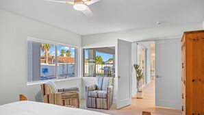 A bedroom with a large bed, two striped armchairs, a wooden wardrobe, and a view of the outside. - El Dorado by Avantstay Luxe 4BR w/ Pool, Putting Green, Fireplace Near Kierland (Scottsdale)