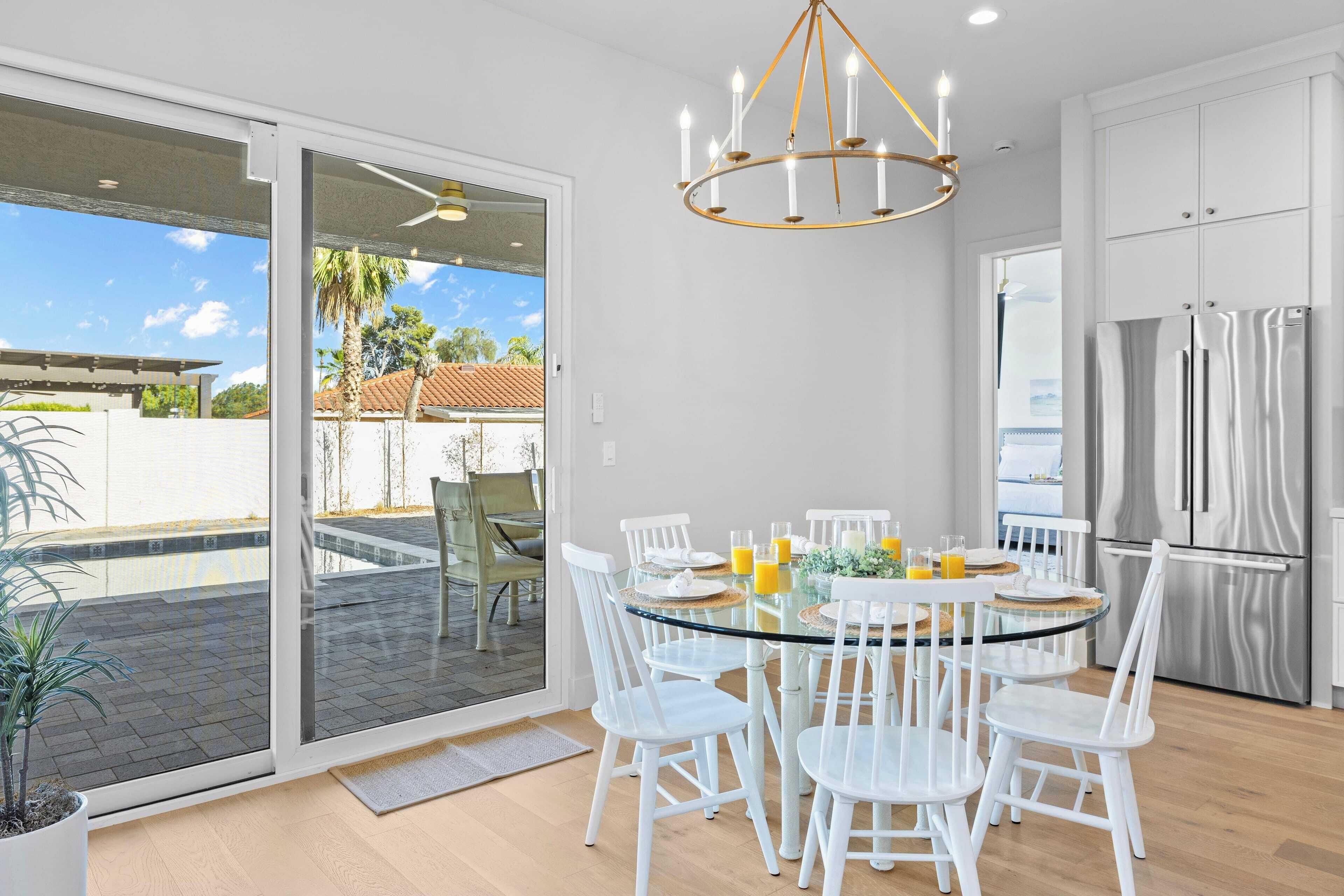 A modern kitchen with a glass dining table, white chairs, and stainless steel appliances.