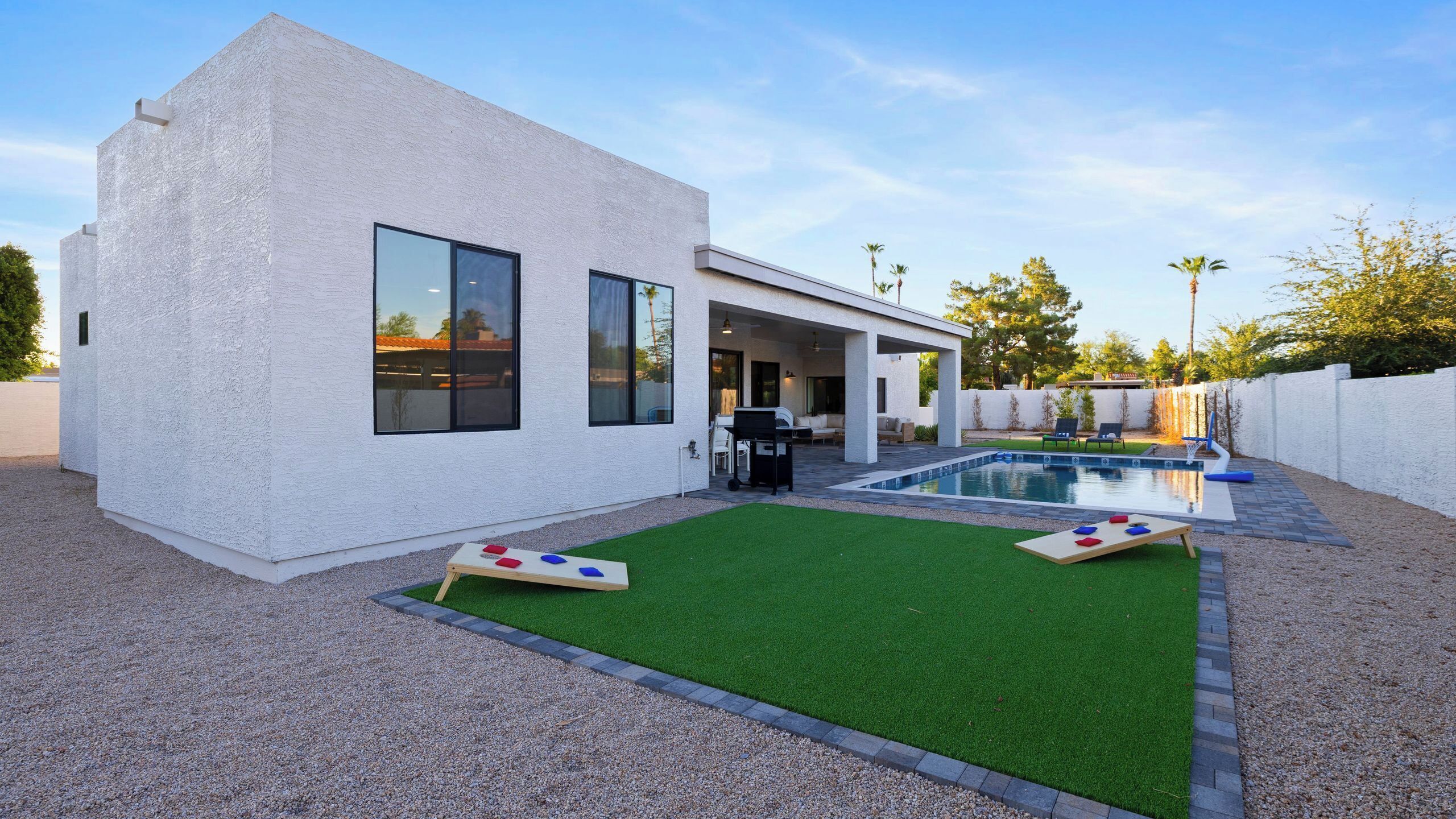 Et moderne hus med swimmingpool, terrasse med udendørs møbler og en velplejet græsplæne.
