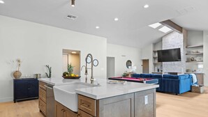 A modern kitchen with a central island, wooden cabinets, and a built-in TV. - El Dorado by Avantstay Luxe 4BR w/ Pool, Putting Green, Fireplace Near Kierland (Scottsdale)