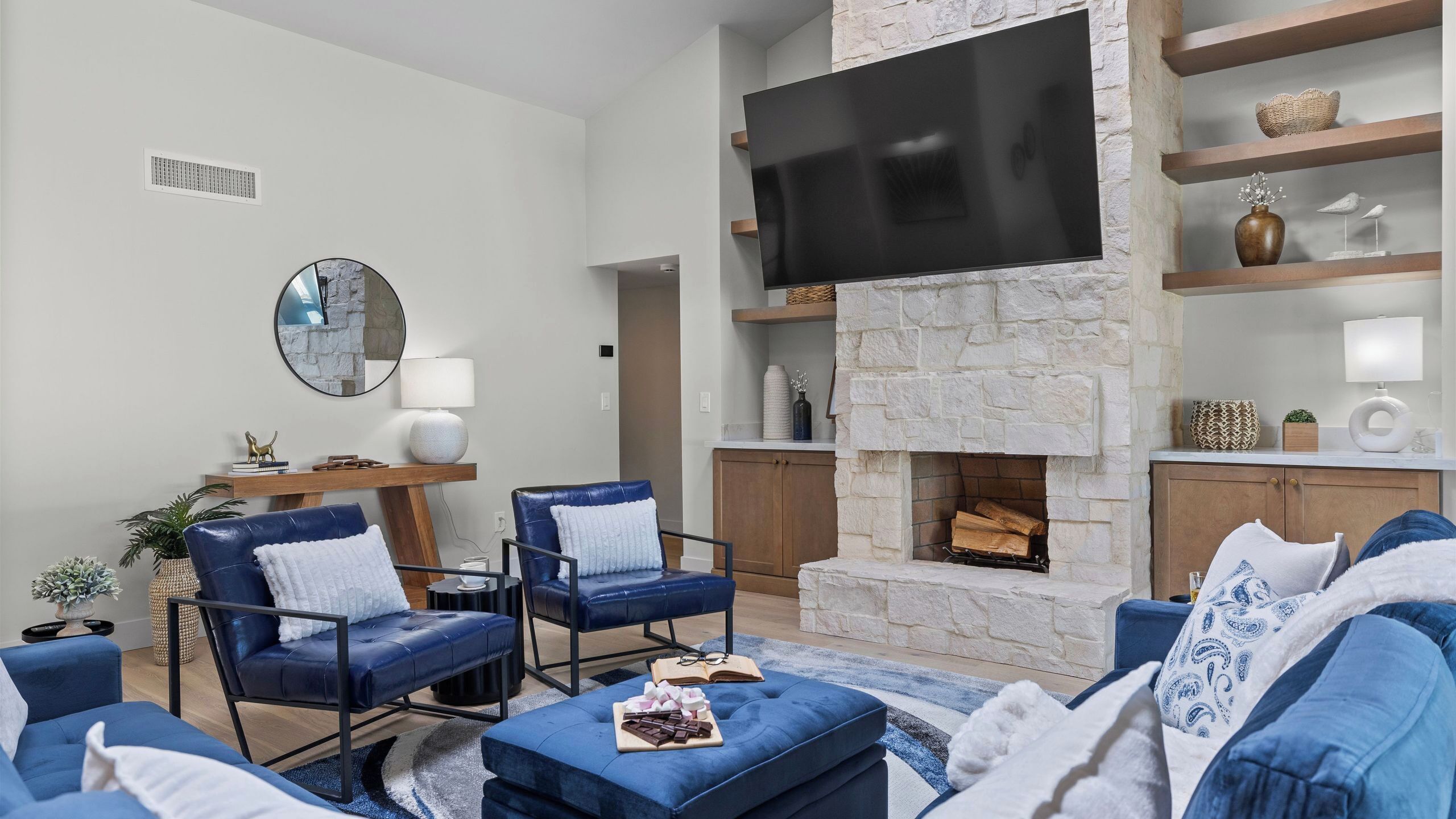 A living room with a stone fireplace, a flat-screen TV, leather chairs, and a sofa.
