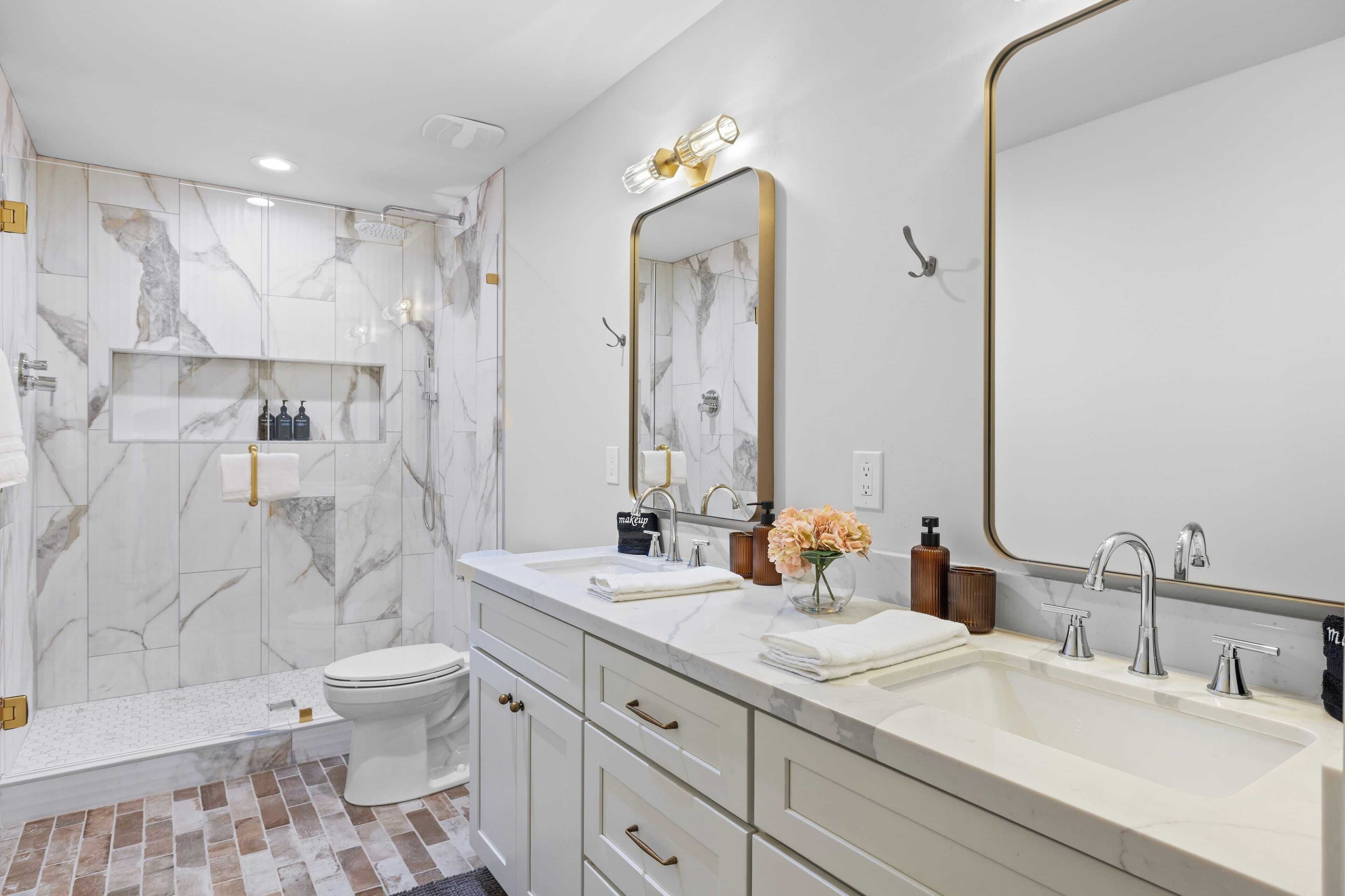 Une salle de bain moderne avec un pare-baignoire en marbre, un grand miroir, deux vasques et un espace douche.