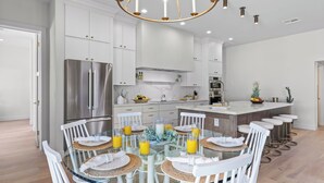 A modern kitchen with white cabinetry, stainless steel appliances, and a central island with bar stools. - El Dorado by Avantstay Luxe 4BR w/ Pool, Putting Green, Fireplace Near Kierland (Scottsdale)