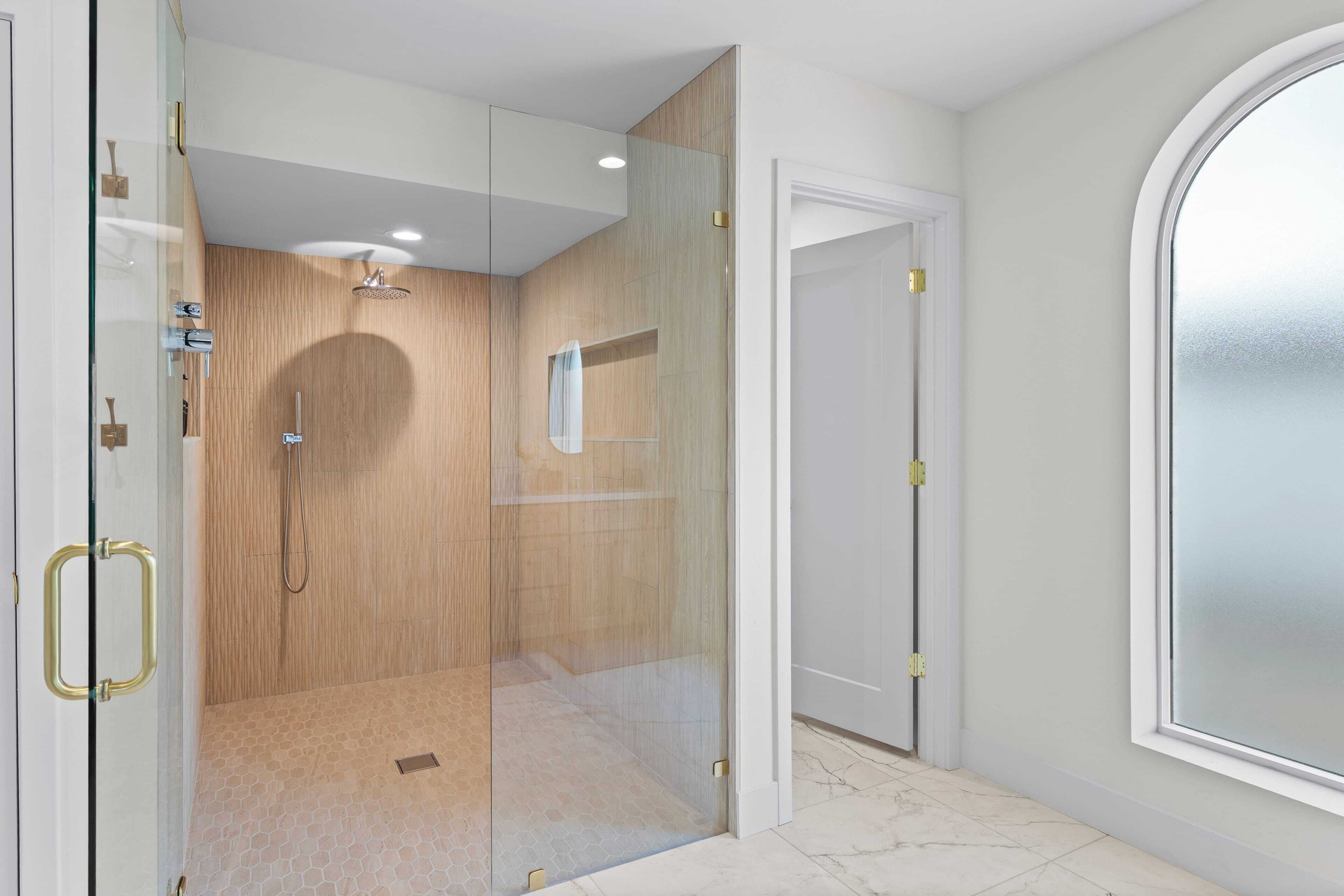 Un baño moderno con ducha envuelta en vidrio, tocador de madera y un ventanal grande.