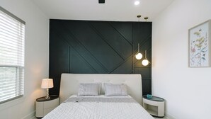 A modern bedroom with a large bed, a dark accent wall, bedside lamps, and a small table with a clock.